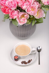 A cap of coffe with sweet and coffee beans near the vase with flowers