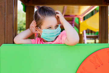 child girl in a mask is playing on the playground outdoors     