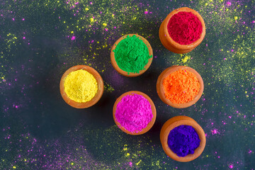 Eco-friendly colorful holi powder or gulal in earthen pot on black background.