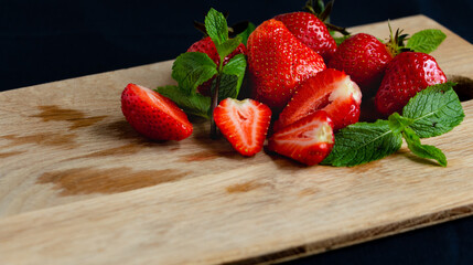 Appetizing juicy bright strawberries on a kitchen wood board on a black background with branches of fresh mint