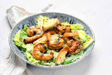 Classic caesar salad with grilled shrimps on gray background.