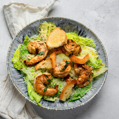 Classic caesar salad with grilled shrimps on gray background.