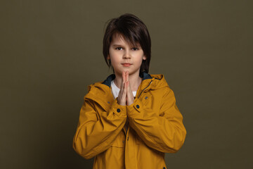 Cute little boy 1keeps palms pressed together having regretful look, asking for forgiveness....