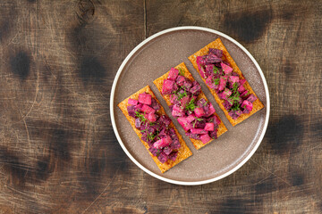 Bruschetta with pickled beet, apple and mayonnaise. Sandwich or crostini on a serving plate on a brown background. Crusty bread with traditional Scandinavian beetroot salad
