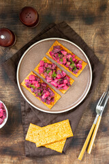 Bruschetta with pickled beet, apple and mayonnaise. Sandwich or crostini on a serving plate on a brown background. Crusty bread with traditional Scandinavian beetroot salad