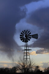 windmill at sunset that's surrounded by clouds with a tree north of Hutchinson Kansas USA out in the country.
