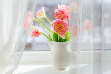a vase of pink tulips  on the window