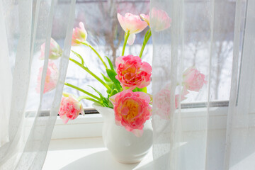 a vase of pink tulips  on the window
