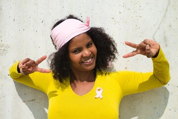 very happy african-american woman with a pink scarf and yellow t-shirt on grey background