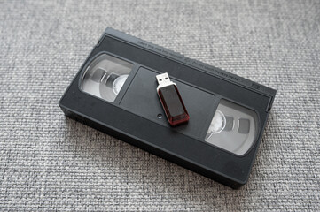 Old tape video cassette with usb flash disk on gray knitted background