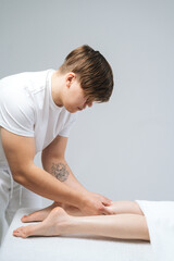 Side view of male masseur massaging lower part of leg to young unrecognizable woman in spa salon. Professional therapist men doing wellness massage shins and legs for female client.