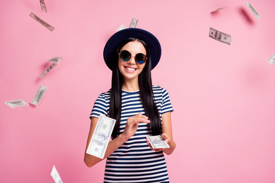 Photo portrait of girl with stacks of money throwing cash isolated on pastel pink colored background with flying dollars