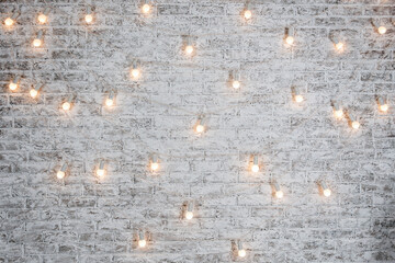 Light bulbs on white brick background. Vintage edison light bulbs garland in loft interior. Rustic...