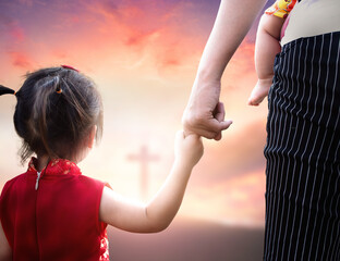 Child's hand holding mother's finger on blurred cross background.