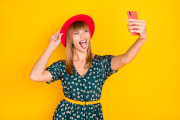 Portrait of lovely crazy cheerful girl taking selfie posing touching hat showing tongue tease isolated over bright yellow color background