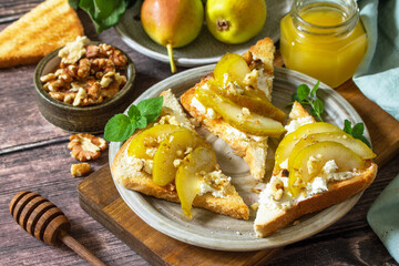 Summer healthy breakfast or snack, antipasto. Grill toast with caramelized pear, honey, nuts and cheese ricotta on a wooden rustic table.
