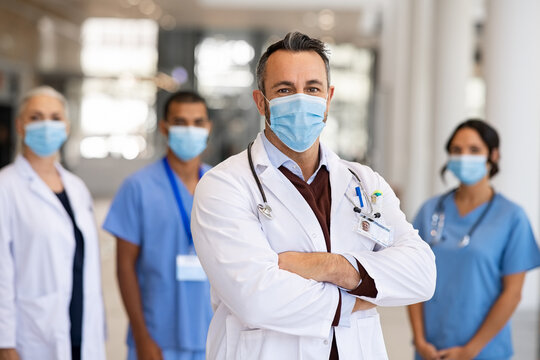 Mature proud doctor with face mask and his medical team in background