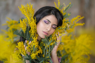 Portrait of a gentle dark-haired girl enjoying a bouquet of mimosa