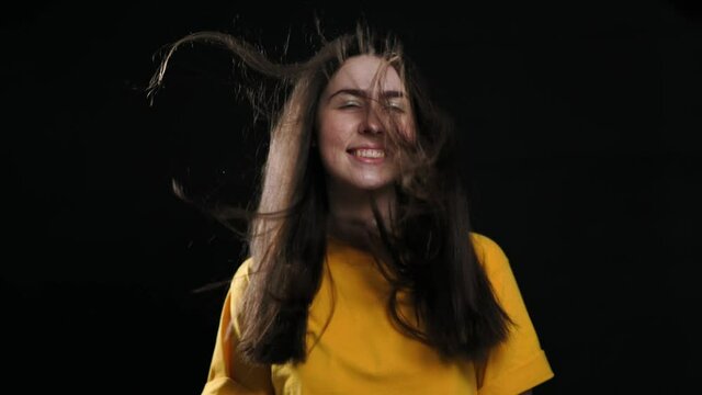 A young smiling caucasian girl and her hair from below blows the air. Slow motion. Black background