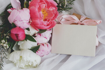 Stylish greeting card, peonies bouquet, gift box on soft white fabric. Happy Mothers day. Copy space
