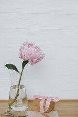 Beautiful peony flower in vase, gift box, greeting card, scissors on wooden background, copy space