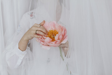 Beautiful stylish woman behind soft tulle holding peony in hands. Sensual aesthetics. Womens day