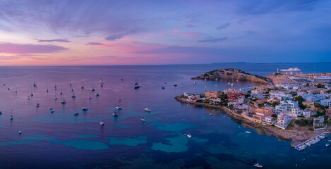 Amazing sunset in Ibiza Spain with orange and violet sky and boats floating on the sea and coast view of the town © Pawel