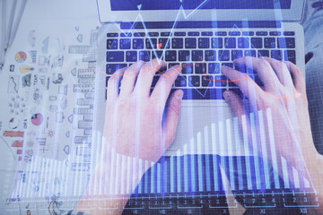 Double exposure of man's hands typing over laptop keyboard and forex chart hologram drawing. Top view. Financial markets concept.
