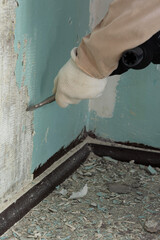 Worker removes old paint from a concrete wall with a rotary hammer with a chisel, a mechanical method of removing paint, repair work in an apartment