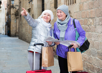 Happy mature ladies travellers with suitcases visiting sights of European city with map