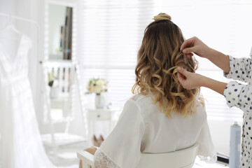 Obraz na płótnie Canvas Professional stylist making wedding hairstyle for bride in salon, back view