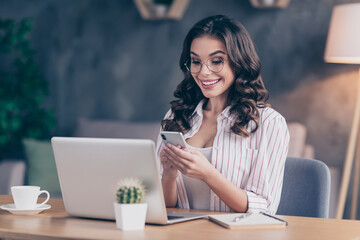 Photo of funny pretty young lady wear white shirt spectacles typing modern gadget sitting table indoors inside room home