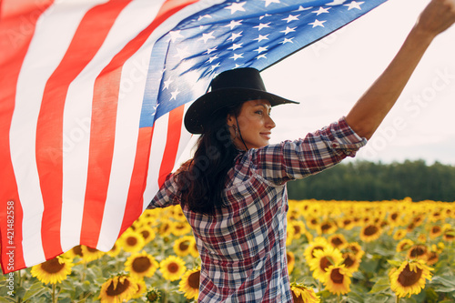 Young woman with American flag in the sunflower field. Harvest USA concept.