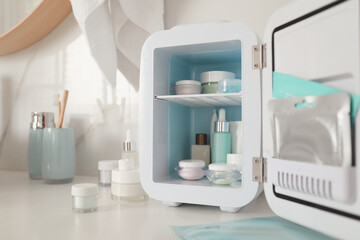 Cosmetics refrigerator and skin care products on white table indoors, closeup