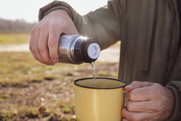 Fototapeta na wymiar Man pouring hot drink into mug from thermos outdoors, closeup