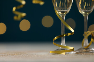 Glasses of champagne and serpentine streamers on table against blurred lights, closeup
