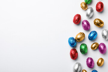 Chocolate eggs wrapped in colorful foil on white background, flat lay. Space for text