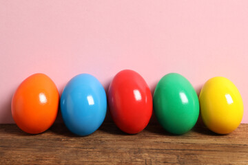 Easter eggs on wooden table against pink background