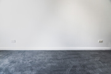 empty room with brand new grey blue carpet laid on the floor and freshly painted white walls, home...