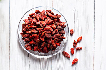  Dried goji berries in a glass plate on a white wooden table. Composition with organic, natural, Chinese wolfberries. Superfoods.
