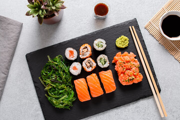 Sushi takeaway with sushi set, wakame salad, chopsticks and sauces on gray concrete background, top view