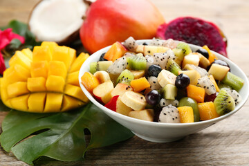 Delicious exotic fruit salad and ingredients on wooden table