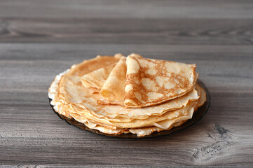 There is a plate of pancakes on the wooden table. Image with selective focus.