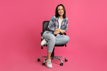 Fototapeta na wymiar Mature woman sitting in comfortable office chair on pink background