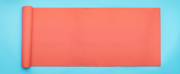 Minimal exercise and concept with pink fitness yoga mat on blue background. Horizontal banner size flat lay.