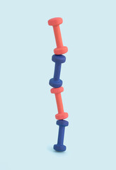 Pink and blue exercise dumbbell weights stacked into gravity defying tower for unique, minimal fitness concept.