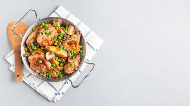 Chicken with potatoes, mushrooms and green peas, in metal pot, horizontal, top view, copy space