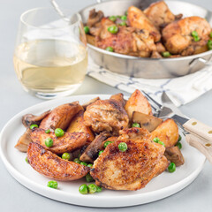 Chicken with potatoes, mushrooms and green peas, on a white plate and in metal pot, square format