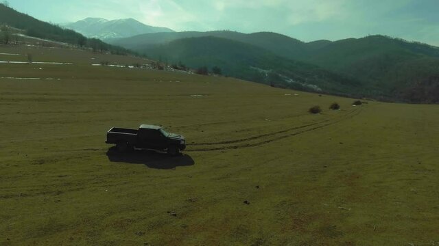 Off Road pickup truck driving on grass field and sunset landscape with mountains. Drone Aerial landscape footage.