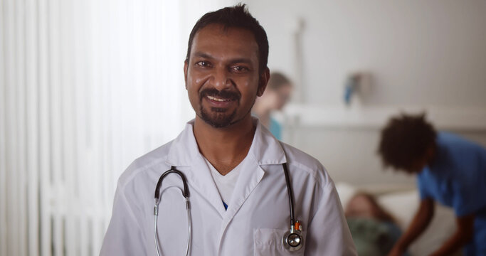 Portrait Of Mature Indian Doctor Looking At Camera And Talking In Hospital Ward